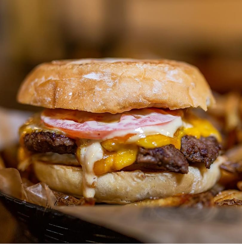 Gourmet cheeseburger with melted cheddar, tomato, and creamy sauce on a rustic bun.