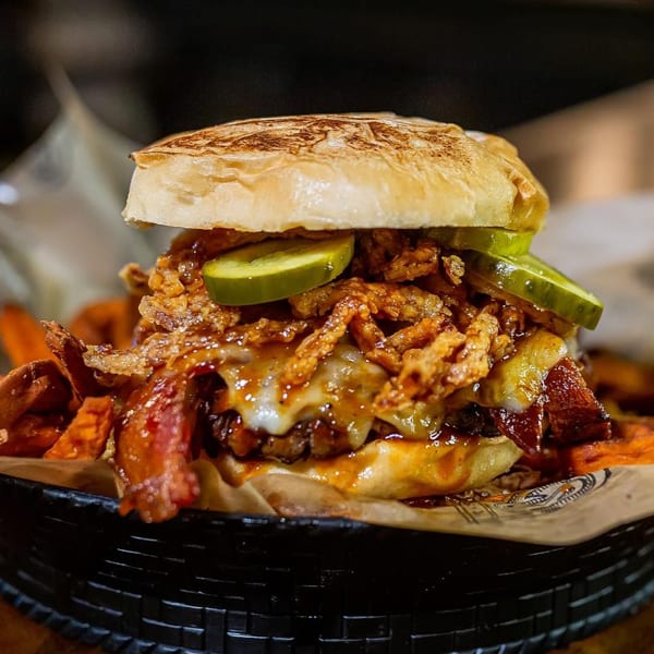 A loaded burger with melted cheese, bacon, crispy onions, pickles, and sweet potato fries.